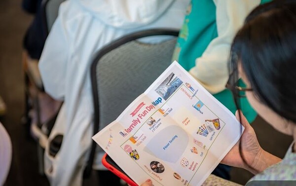 아이들이 인형극 관람하는 동안 한 어머니가 Family Fund Day program map을 보고 있다. 